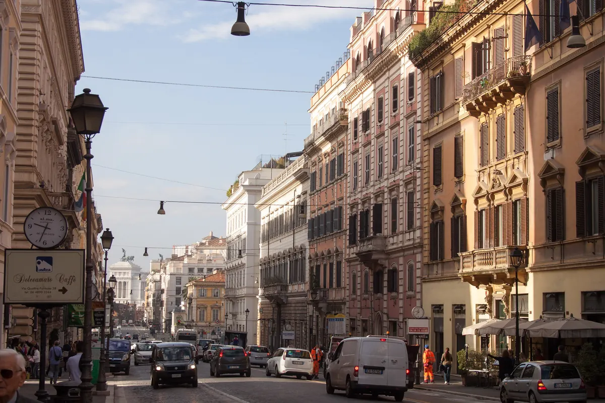 Via Nazionale in Rome in afternoon light, a long street of tall ochre and pink palazzi with balconies, running toward a white monument in the distance.